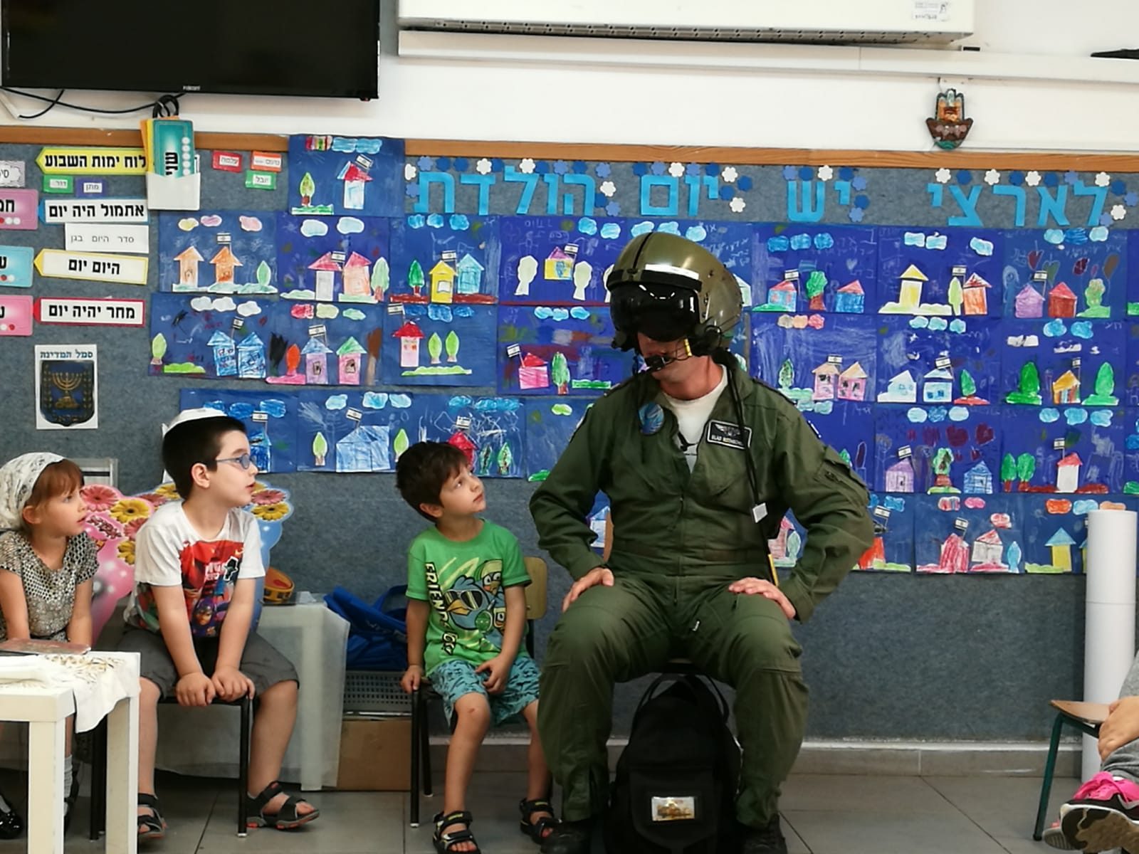 Elad kneeling with a child, holding his flight helmet